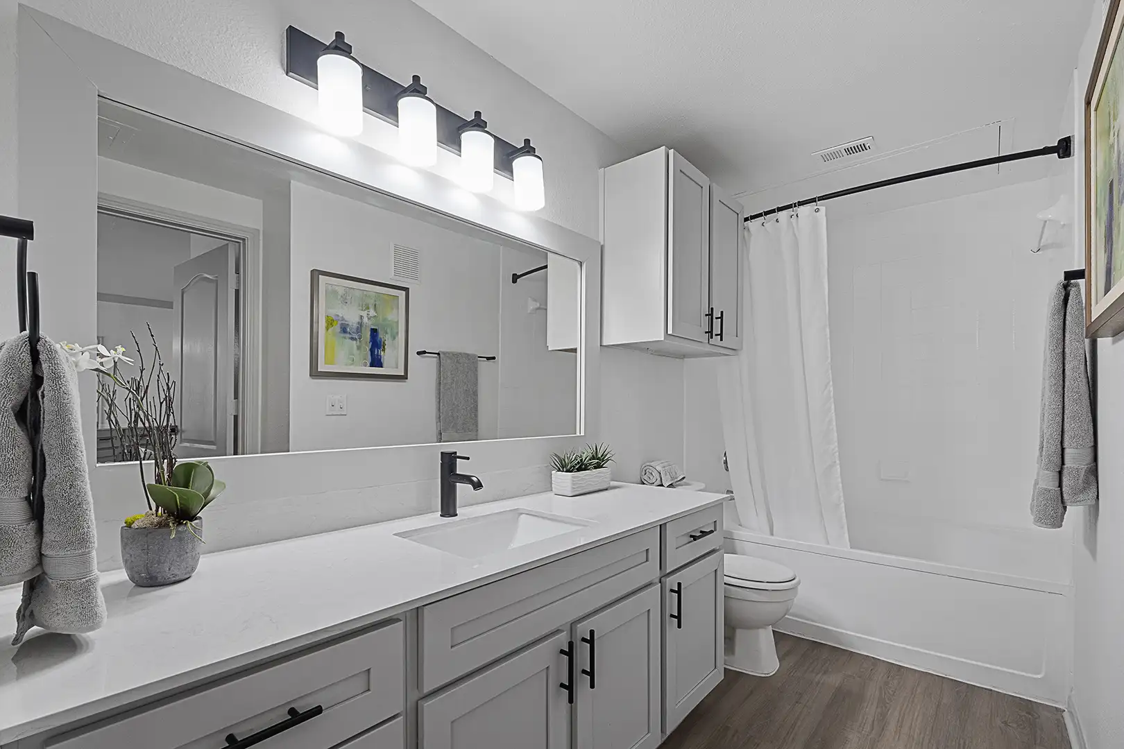 model bathroom with plank flooring, ample lighting and white cabinetry